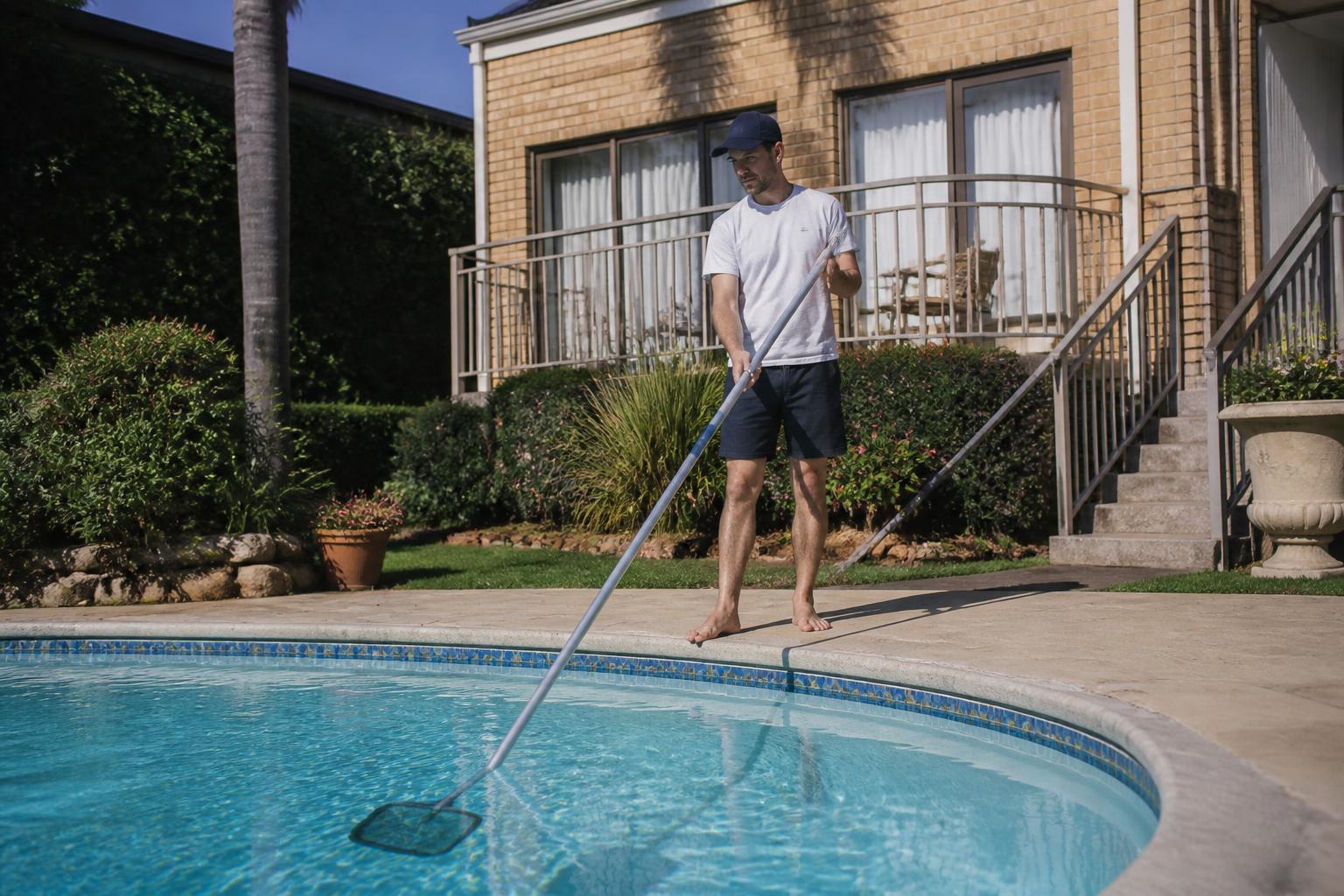 Friendly local pool maintenance specialist cleaning a sparkling suburban pool in Cape Town